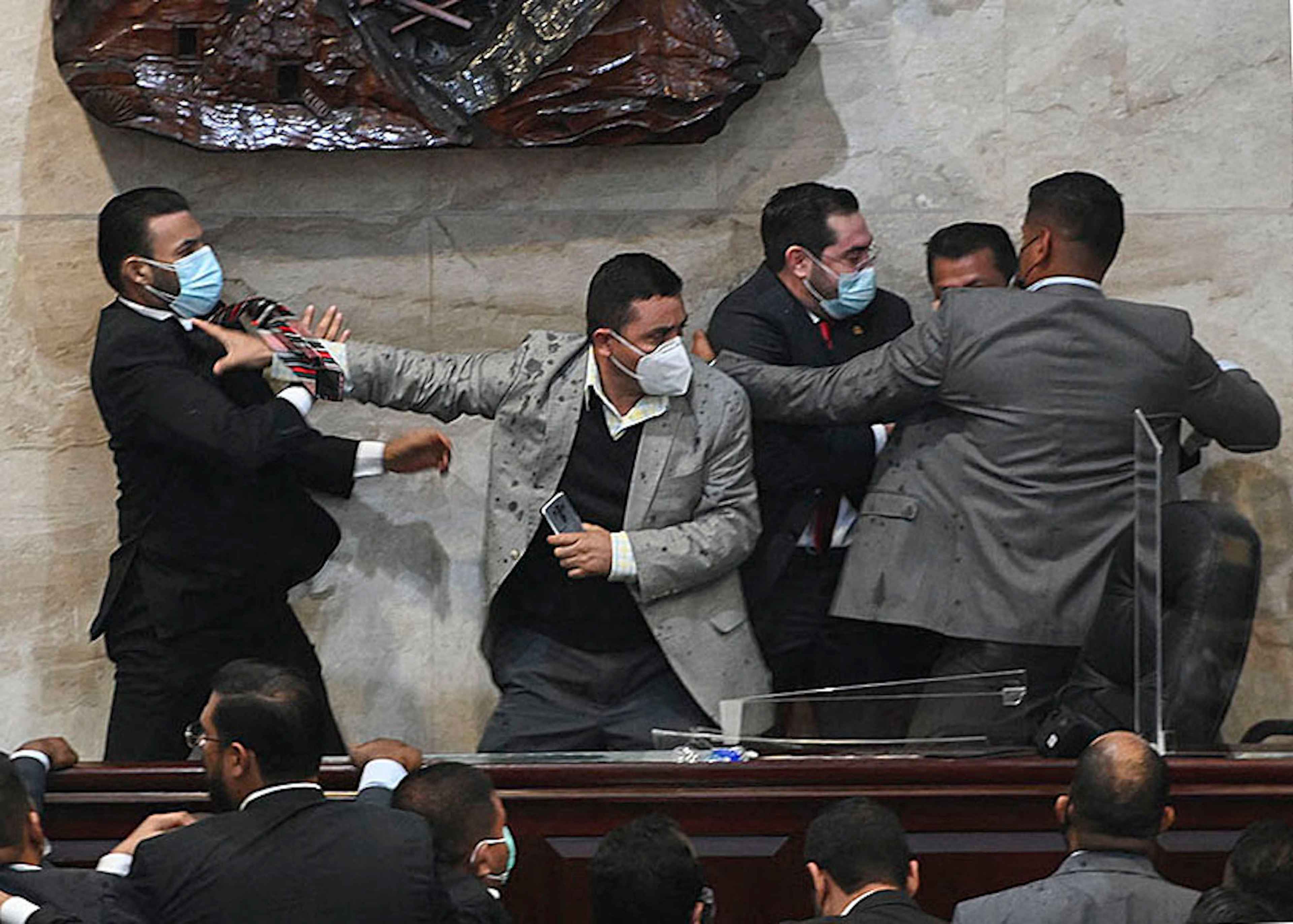 Deputy for the Liberty and Refoundation (Libre) party Rassel Tome (left) tries to assault deputy Jorge Calix (second to the right) after his election as President of the Provisional Board of Directors of the National Congress, at the Legislative headquarters in Tegucigalpa, on January 21, 2022. The Honduran Congress elected its provisional board of directors in the midst of a brawl, with blows and shoves, because 20 members of the party that won the November presidential elections rebelled against the new President Xiomara Castro. Photo Orlando Sierra/AFP