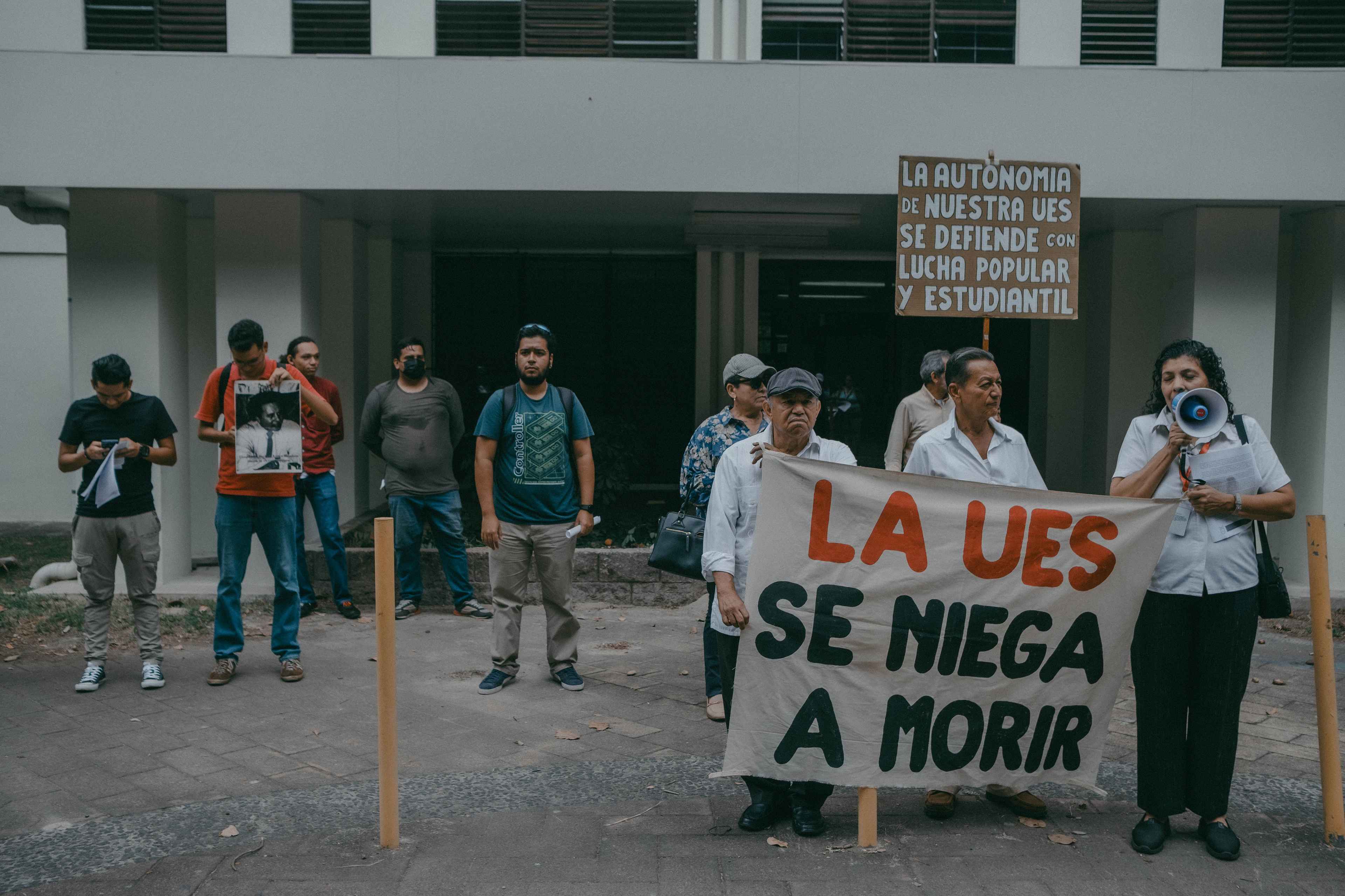En noviembre del 2018, Nayib Bukele asistió a la Universidad Nacional como parte de su campaña presidencial. Durante el discurso, el entonces candidato de Gana, dijo que convertiría a la UES en la mejor universidad de Centroamérica. Más de cinco años después de esa promesa, la realidad es diferente para la única universidad pública del país. En su interior ahora se habla de miedo. "El miedo se ha apoderado de toda la gente aquí", decía en voz baja uno de los asistentes a una marcha, el 27 de mayo de 2024, en rechazo al uso de las instalaciones de la UES para fines no académicos. La marcha fue convocada por la comisión especial "La UES se Niega a Morir" y asistió apenas una docena de personas, entre estudiantes y catedráticos. el mismo rector de la UES admite que "hay miedo de expresarse". La comisión fue creada en febrero del 2024 para exigir la autonomía de la universidad y denunciar la crisis por la deuda acumulada del Gobierno, que ya asciende a 51.3 millones de dólares. También exigieron la recuperación completa de los edificios del campus central en los que cuatro facultades tienen sus aulas y los estudiantes no asisten a clases presenciales desde 2020. Mientras tanto, en febrero de 2024, La Villa Olímpica de la Universidad de El Salvador albergó a militantes del partido Nuevas Ideas para trabajar en el escrutinio final de las elecciones presidenciales y legislativas. En febrero de 2024, a pesar de la deuda, el Gobierno volvió a utilizar las instalaciones para hospedar a "periodistas" que cubrirían la toma de posesión inconstitucional de Bukele. Foto de El Faro: Carlos Barrera.