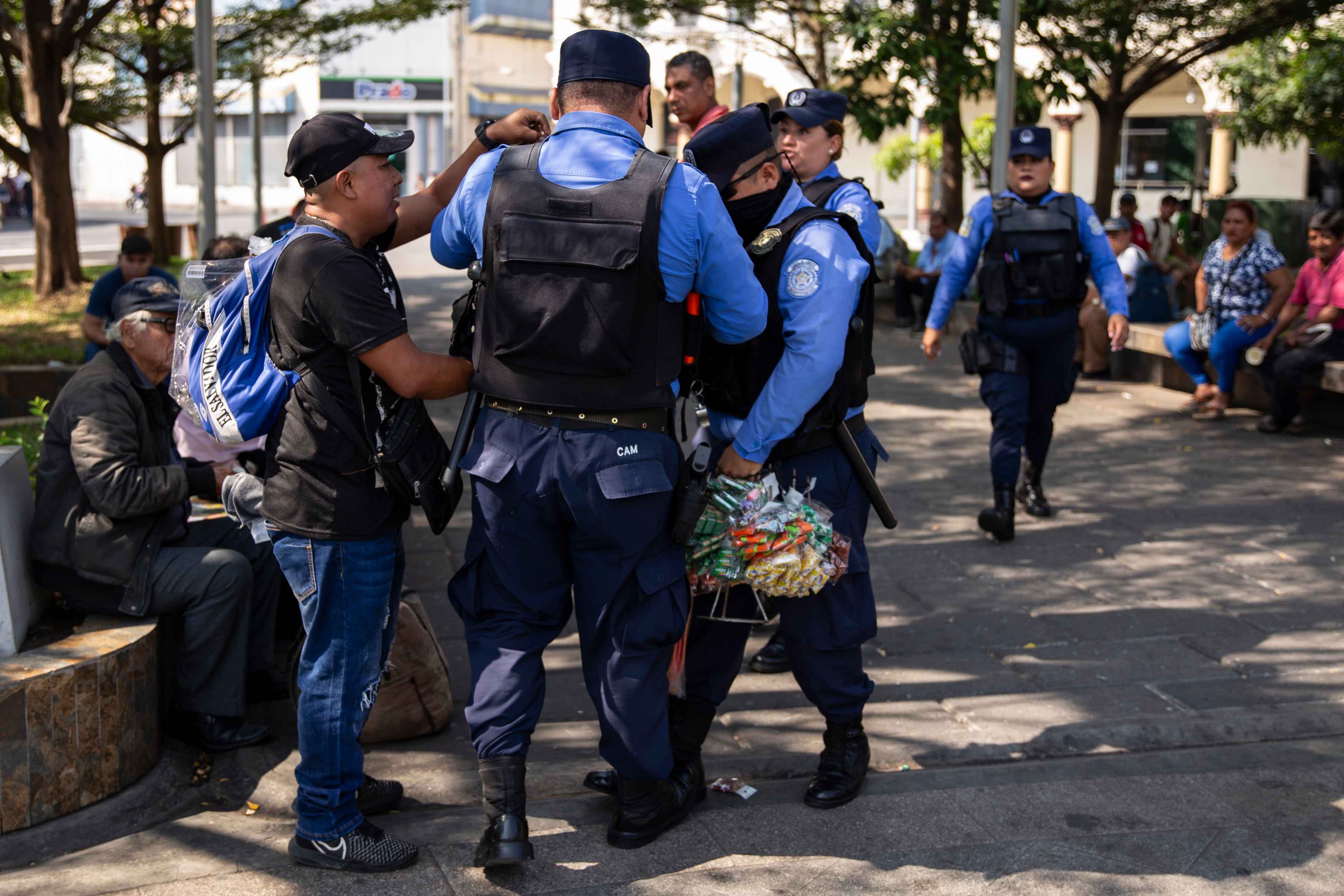 Tres agentes del CAM lo despojaron de su venta, rompieron las bolsas y lastimaron su dedo medio de la mano izquierda mientras algunos dulces cayeron al suelo de la plaza Libertad, en el Centro Histórico de San Salvador. “Estos son traidores”, dice Mario René Castro, de 40 años, quien vende dulces desde hace un año cuando perdió su empleo. "Nunca me advirtieron, me cayeron de sorpresa y me robaron mis $50 de venta", dijo Mario mientras se frotaba el dedo lesionado. Mario es habitante del barrio San Jacinto, en San Salvador. Todos los días vende dulces en las paradas de autobuses, en los municipios de Zacatecoluca y San Marcos, cerca de los hospitales, en el mirador de Los Planes de Renderos y en algunos espacios turísticos. El domingo 14 de febrero de 2024 decidió bajar al centro de la capital, cuyas cuadras principales son emblema turístico de la administración Bukele. Cientos de vendedores han sido desalojados de esas calles sin tener opcion alguna. Muchos intentan aún vender de forma ambulante, en carretones o cargando la venta, y huyendo del CAM que los persigue para mantener la imagen de un Centro ordenado, limpio y sin venta alguna. Todo esto ocurre en un país donde, desde 2019 que Bukele llegó al poder, más de 210,000 personas han caído en la categoría de pobreza extrema. Foto de El Faro: Víctor Peña.