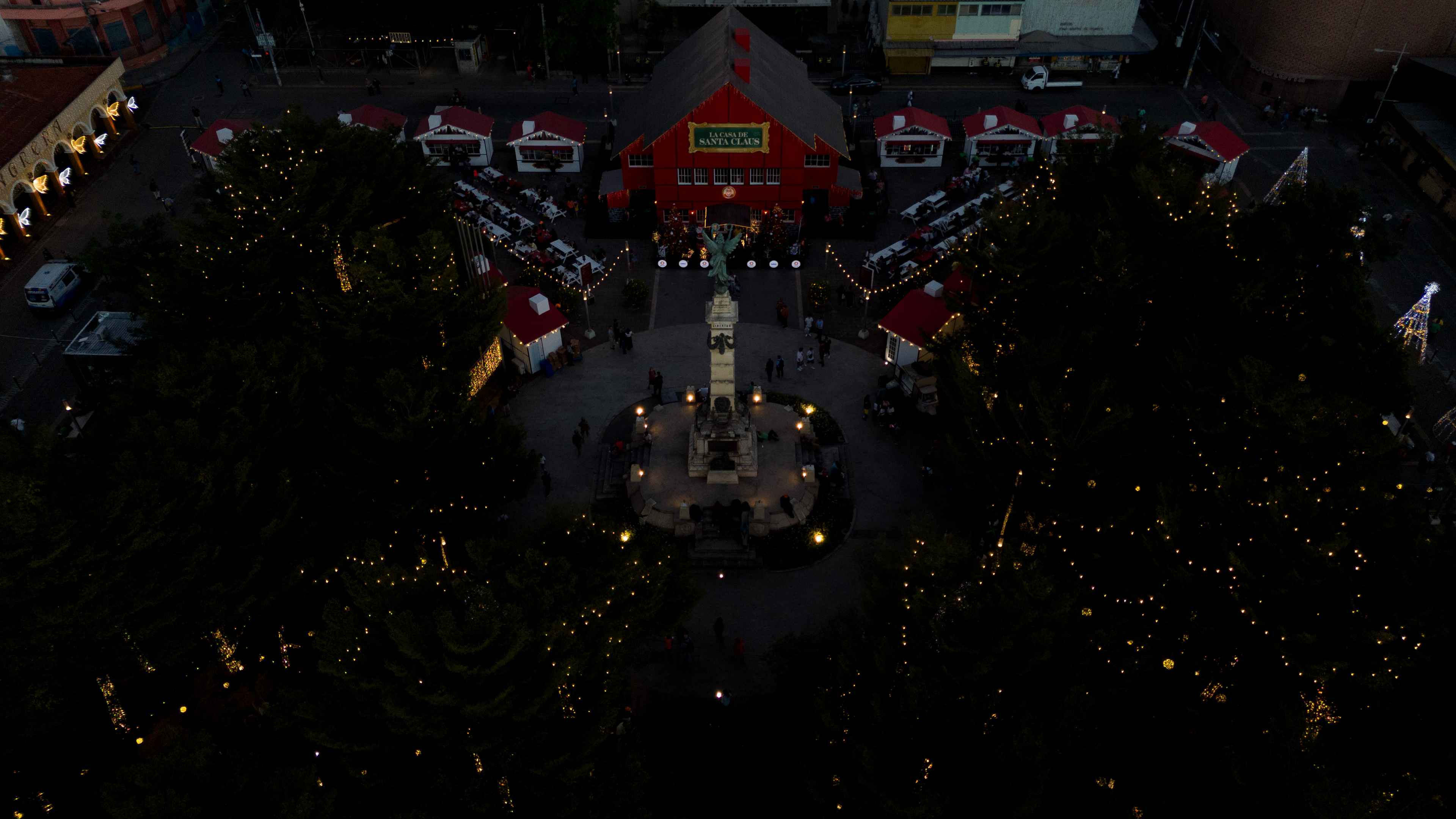 El monumento de la Plaza Libertad está rodeado de una villa con una casa que se erige en el centro. Al frente de la gran casa roja el rótulo de "La Casa de Santa Claus" da la bienvenida. En la base de la casa, unos rótulos digitales dan publicidad al bitcoin. Decenas de personas atraídas por las luces y la comida abarrotan la plaza. Este espacio público está prohibido para los vendedores ambulantes que se ganan la vida ofreciendo productos en el Centro Histórico. Foto de El Faro: Carlos Barrera 