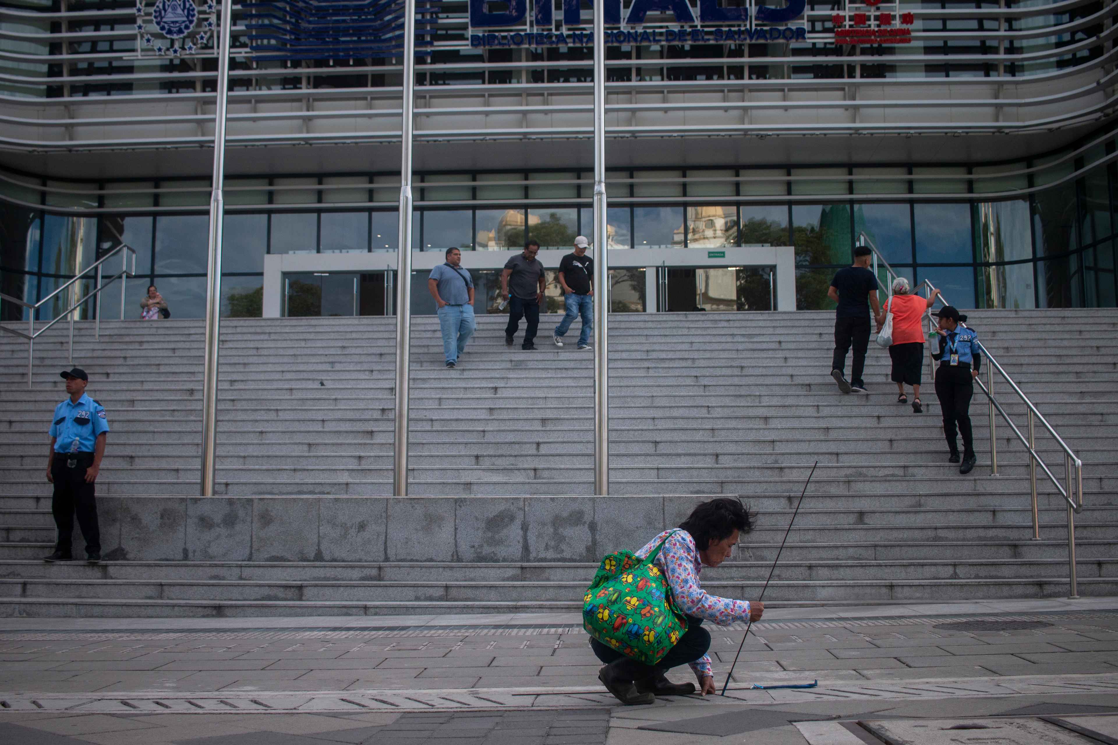 José picks up coins in front of the National Library. He walks along the edges of the streets of the Historic Center to detect coins trapped under the tiles that cover the drains. He is 70 years old and is a do-it-all, “a day laborer with a sickle and a paintbrush,” as he calls himself. When he finds no work for the day, he collects coins with the help of two iron rods, with bent blades at the ends, which penetrate into the slots where his hands cannot fit. In about half an hour, José found coins totalling $0.52. “It was better when all those [informal vendor] shacks were here. There was more money lying around,” he recounts as he battles for 20 minutes to salvage a $1 coin in front of the National Library of El Salvador. “I don’t always find lots of the ones I want. But I'm poor, and that's why I do this,” he says amid the hustle and bustle of the installation of the ice rink and Christmas Village. Photo Víctor Peña