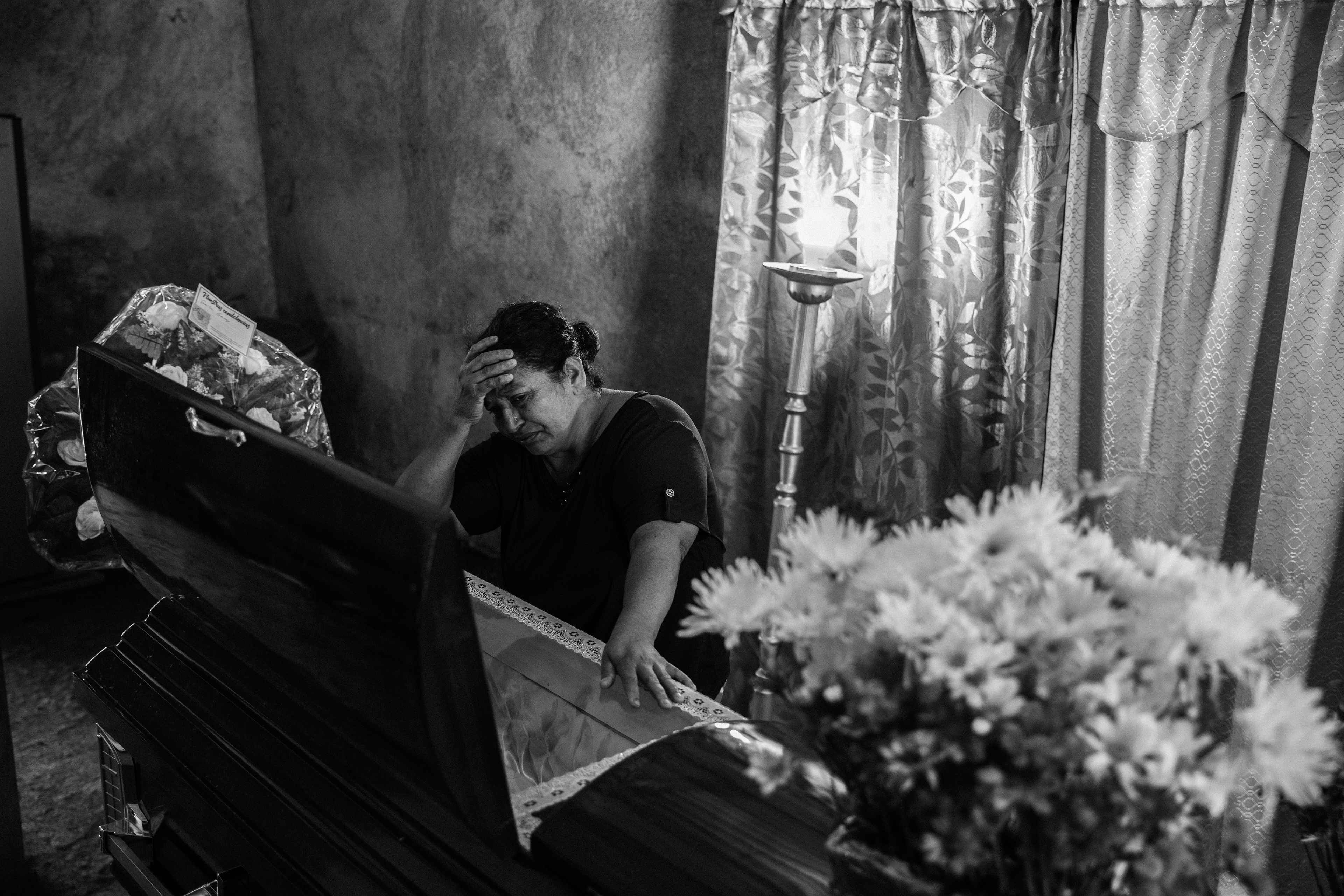 María Elena llora junto al ataúd de su hijo. El 5 de octubre de 2022, su hijo, Marvin Díaz, fue capturado en una zona rural de Usulután, El Salvador. En la cárcel, debido a las condiciones insalubres, enfermó. El 6 de junio de 2024, el tribunal le concedió la libertad después de que las fotografías de Marvin, encadenado a una cama de hospital, se hicieran virales en redes sociales. Marvin falleció el 28 de julio de 2024 tras no recibir un tratamiento adecuado en el tiempo necesario.